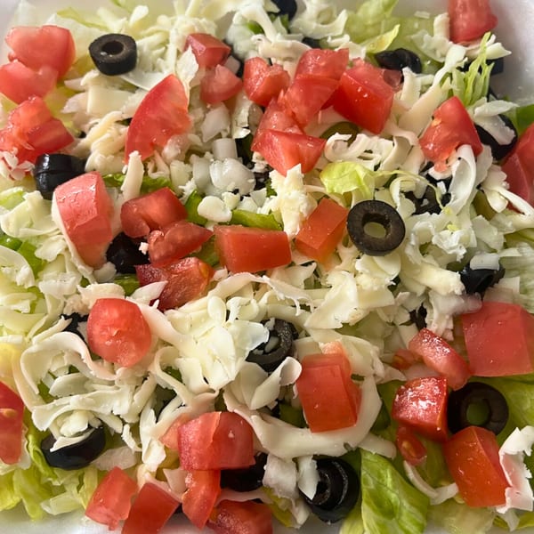 Close-up of a fresh salad with shredded lettuce, diced tomatoes, black olives, and white cheese.
