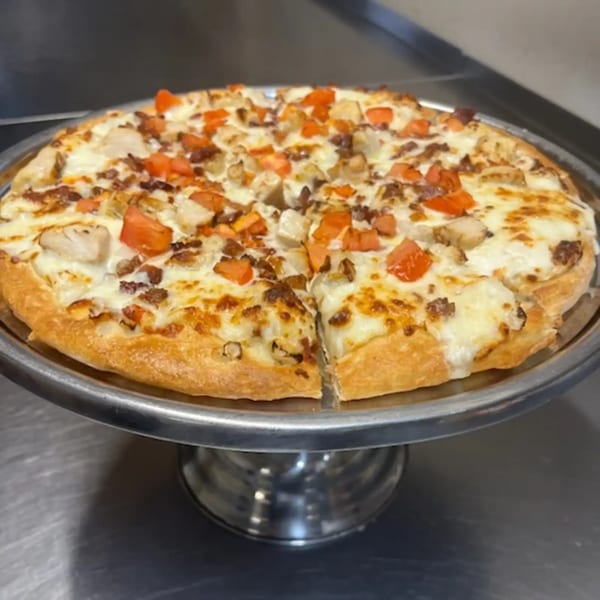 Cicero's Pizza with white sauce, chicken, bacon, and diced tomatoes on a metal stand.