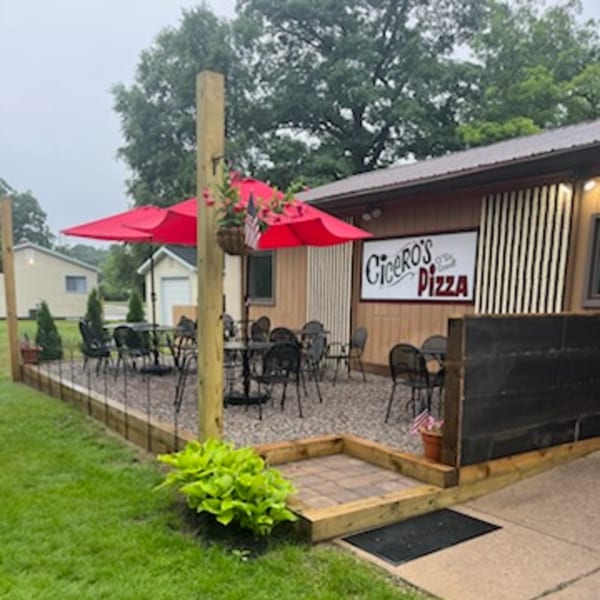 Cicero's Pizza outdoor patio with black tables, chairs, and red umbrellas on a gravel surface.