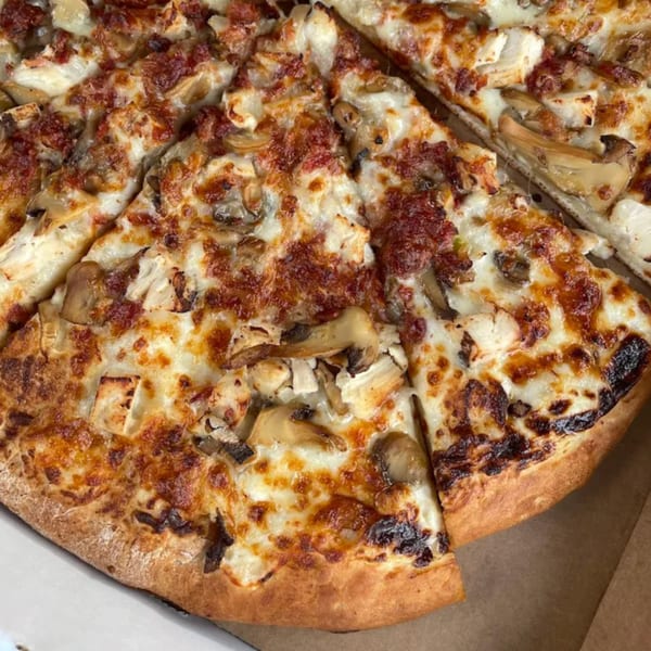 Close-up of a sliced Ciceros Pizza with melted cheese, mushrooms, and other toppings.
